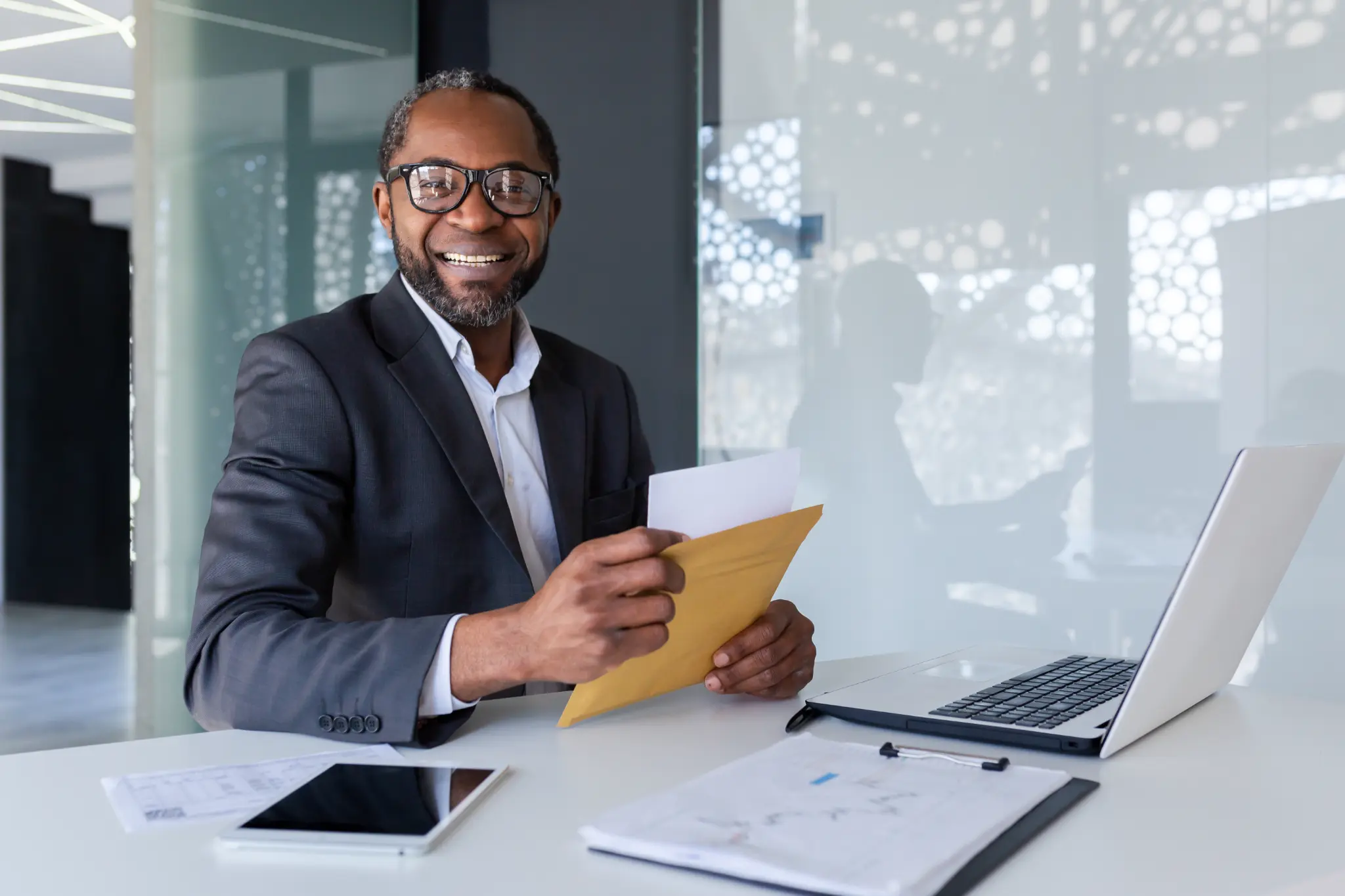 Smiling businessman with glasses holding an envelope at his office desk