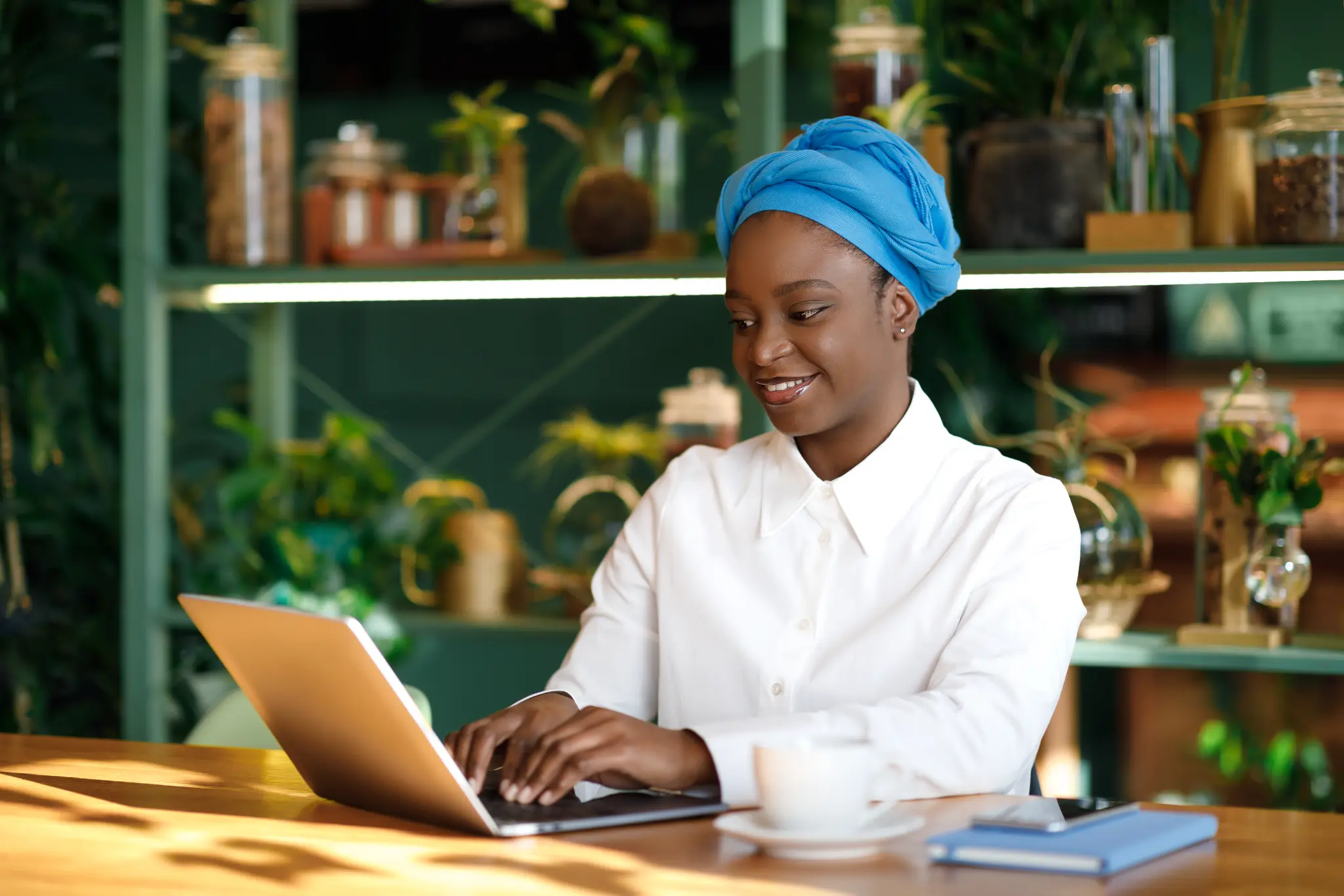 Woman in a blue headwrap working on a laptop in a green café